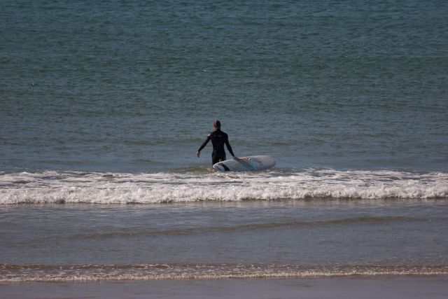 A surfer pulls their board out to sea on Polzeath Beach in Polzeath, Cornwall.