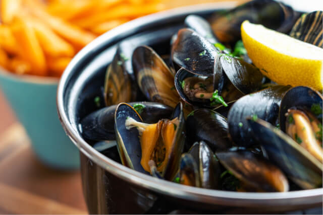 A bowl of mussels with a lemon wedge on top.