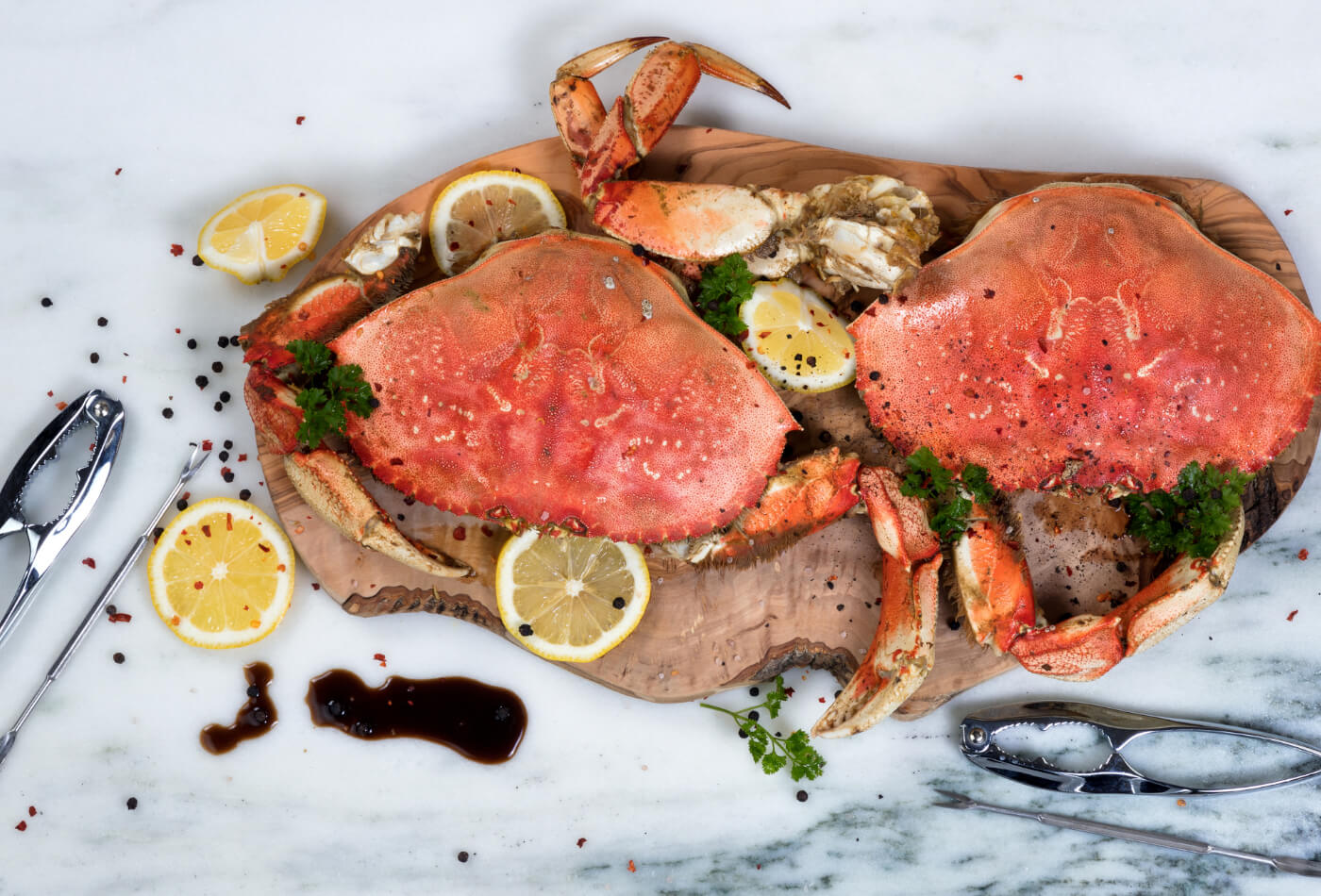 Two cooked crabs on a serving board with wedges of lime and pepper.