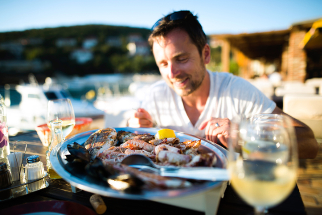 Man on holiday, sitting outside at sunset, eating seafood.