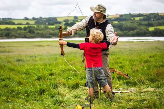 Man teaches a child archery in a field in north Cornwall.