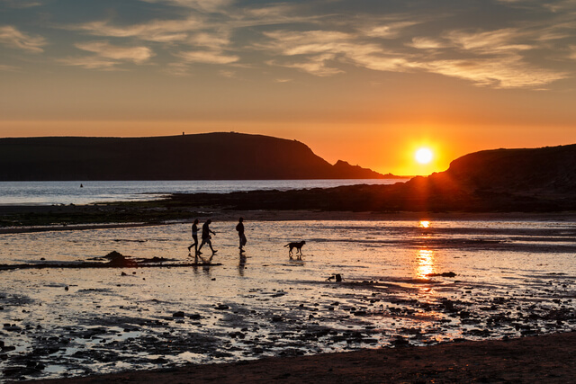 Sunset at Daymer Bay Beach with a family and dog walking along the shore.