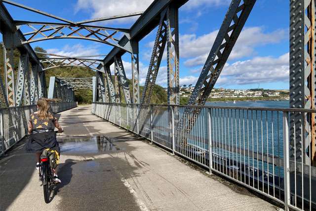 Woman cycling along a bridge on the Camel Trail, with Padstow and the Camel Estuary on the left