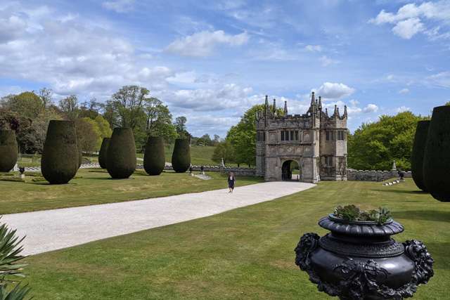 A large gatehouse at the end of an avenue of trees at Lanhydrock, on a sunny day